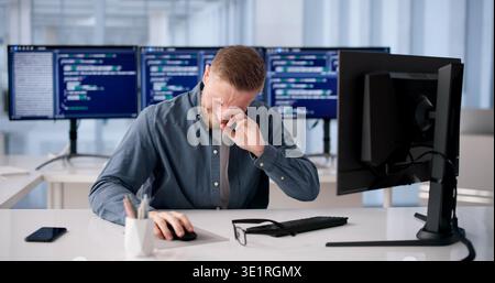 Tired Programmer Rubs Irritated Eye During Long Coding Session At Desk Stock Photo