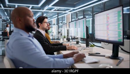 Diverse Team Of Professionals Using Spreadsheets On Desktop Computers Happily. Man And Woman Analysts Studying Reports Stock Photo
