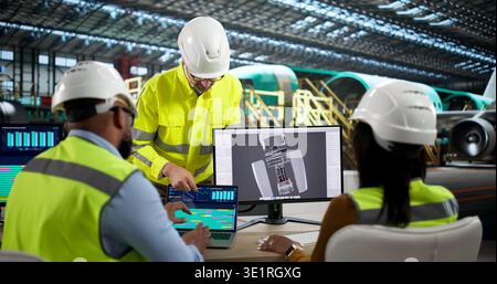 An Engineer And Technician Discuss Jet Engine Repairs Using Laptop Computers. A Diverse Group Stock Photo