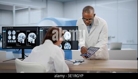 Two Medical Technicians Carefully Study Brain MRI Scans Together Using Computers. A Neurologist Stock Photo