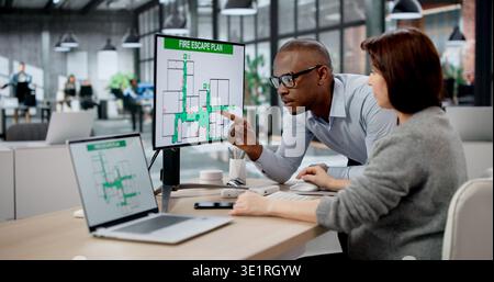 Two People Are Using Laptops In An Office To Create Emergency Safety Plans. A Woman And A Man Collaborate Stock Photo