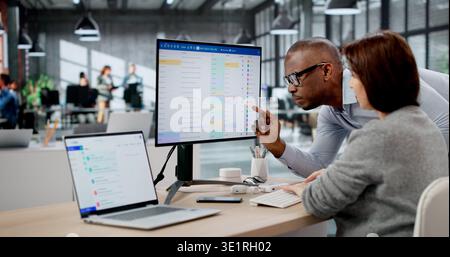 Two Young Professionals, A Woman And A Man, Collaborate On Project Management And Email Software Using Multiple Monitors Stock Photo