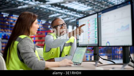 An Industrial Warehouse Worker Uses Multiple Computers To Manage Inventory And Parcels Stock Photo