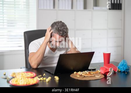 A man suffers from a headache on morning. Tired employee holds his head due to a morning headache. Middle-aged businessman struggles with headache Stock Photo