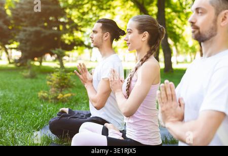 Three friends holding hands in namaste while practicing yoga outdoors Stock Photo