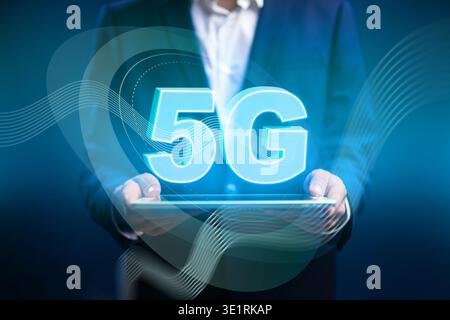 Person displays digital 5G sign on tablet while dressed in formal clothes in dark setting Stock Photo