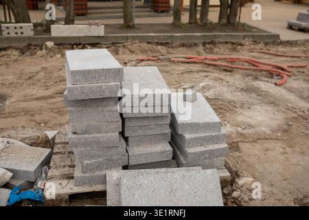 Stack of gray concrete paving stones on wooden pallet at construction site with dirt and tools visible in the background Stock Photo