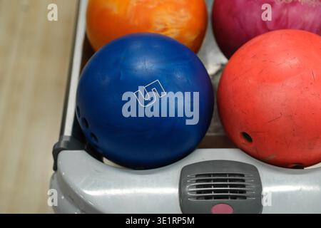 Blue bowling ball with number 5 alongside orange, pink, and red bowling balls on a rack in a bowling alley setting Stock Photo