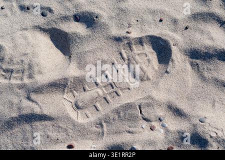 Footprint in fine sand on a beach, showing detailed tread pattern and small pebbles scattered around the imprint Stock Photo