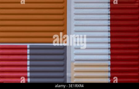 A texture of multi-colored ribbed metal siding with sections in orange, red, gray, white, and beige arranged in a geometric layout Stock Photo