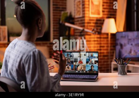Female remote manager participating in online business call from home office. Young self employed woman joins virtual training session on laptop, using hand gesture during her presentation. Stock Photo