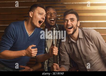 Happy friends singing karaoke together in bar Stock Photo