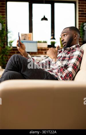 Bearded black man using cellphone for serious video call with business vendors. Focused african american entrepreneur having remote conversation, managing professional negotiations from home. Stock Photo