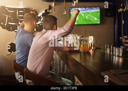 Two friends watching football game and drinking beer Stock Photo