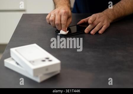 09.20.2025 - Flensburg, Germany. Man cleaning the screen surface of a new Apple iPhone 17pro max with a tissue on dark grey table  Stock Photo