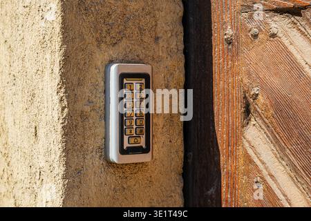 Modern digital door keypad mounted on textured wall beside rustic wooden door, secure access technology detail, selective focus Stock Photo