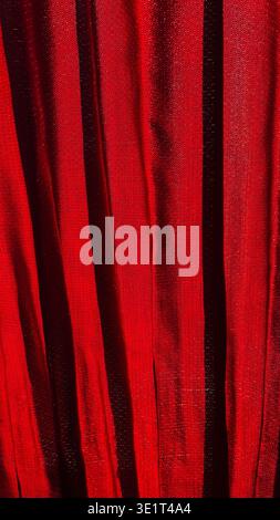 Rich red textile curtain with vertical folds and deep shadows, abstract fabric backdrop, vertical image Stock Photo