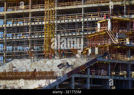 Workers building modern high rise, concrete formwork, scaffolding, tower crane. Industrial construction scene showing teamwork, safety gear, urban development. Stock Photo