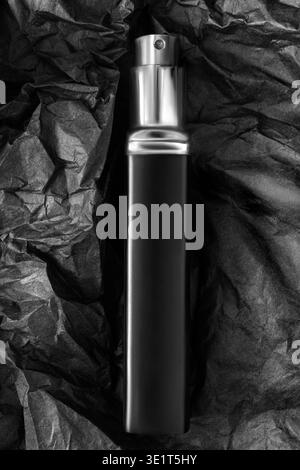 Black perfume atomizer lying on crumpled black packaging paper background Stock Photo