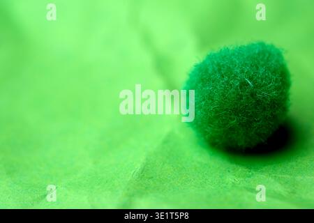 A small, fuzzy green ball sits on crumpled green paper, glowing softly in the light. Stock Photo