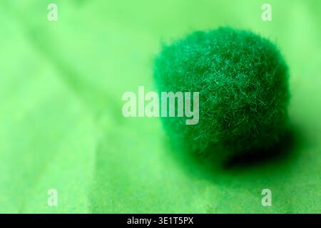 A vibrant green moss ball sits quietly on textured paper, glowing softly. Stock Photo