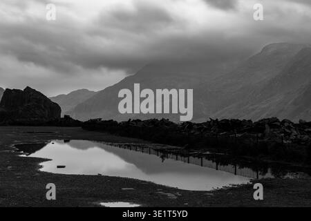 Mount Snowdon and surrounding mountain peaks reflected in still puddle on stony ground in monotone under heavy clouds at Dinorwic slate quarry Stock Photo