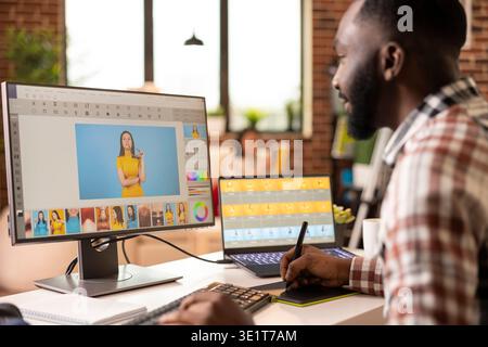 Black male illustrator using stylus and graphic tablet to create digital artwork from home. African american creative designer remotely edits and refines visual content in modern brick wall apartment. Stock Photo