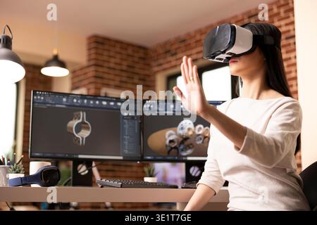 Freelance woman developer immersed in virtual reality, designing precise clamp model. Female engineer wearing vr headset, explores 3d simulation tools to prototype and inspect CAD product designs. Stock Photo