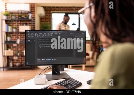 African american freelancer in home office programming an app, reviewing coding scripts and managing tech startup tasks. Self employed woman working remotely online, developing software. Stock Photo