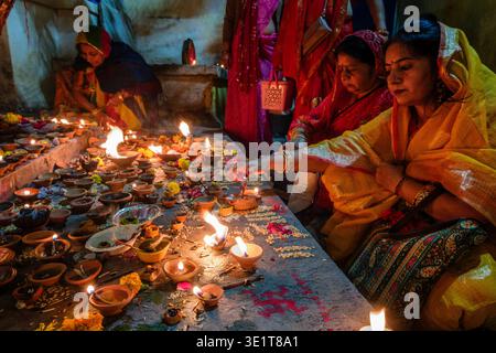 Several women in traditional dress attend to a large collection of burning diya lamps placed on a stone platform during a festival in Udaipur. Stock Photo