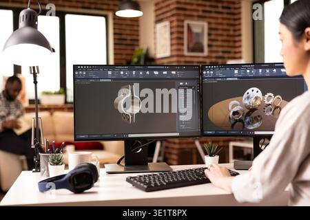 Young female developer working on industrial gear models with dual monitors and computer aided design tools. Creative remote engineer visualizing prototypes in modern home studio. Stock Photo