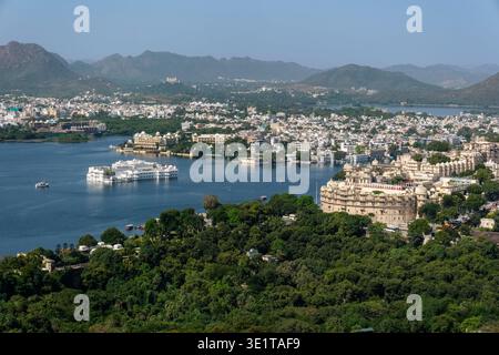An elevated view shows the City Palace and Taj Lake Palace in Udaipur, with the Aravalli Hills stretching across the horizon in the distance. Stock Photo