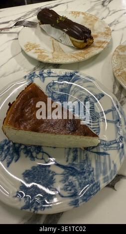 Slice of cheesecake on patterned plate with chocolate eclair in background. Mobile photo Stock Photo