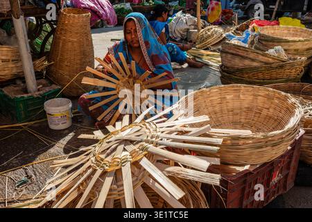 Working at a market in Udaipur, a woman assembles the base of a new bamboo basket, with numerous completed baskets stacked in the foreground. Stock Photo