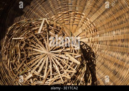 A high-angle close-up shows the intricate radial patterns of hand-woven bamboo baskets stacked at a local craft workshop in the city of Udaipur. Stock Photo