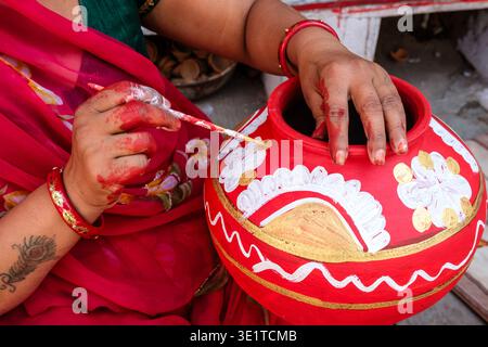 Close-up of a woman in Udaipur decorating a traditional red clay pot with intricate white and gold floral patterns using a small paintbrush. Stock Photo