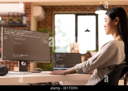 Young woman programmer coding in home office, checking and reviewing machine learning algorithms on device screens. Focused female freelancer working remotely and creating secure web applications. Stock Photo