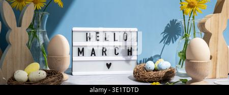 Lightbox with message HELLO MARCH on festive blue background and eco-friendly zero waste natural decoration. Yellow daisies flowers. Bunny egg. Holiday greeting card Stock Photo