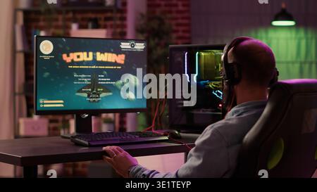Caucasian gamer playing fast paced space shooter simulation enjoying victory after winning difficult gaming competition on pc. Man celebrating feeling victorious in internet multiplayer action game. Stock Photo