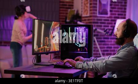 Man streaming multiplayer online first person shooter on pc while gaming girl is fighting in virtual reality game in living room. Gamer playing action rpg simulation while woman uses vr goggles. Stock Photo