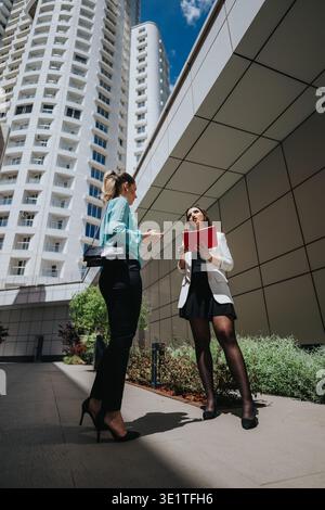 Business collaboration between two professional women discussing plans outside a modern office tower Stock Photo