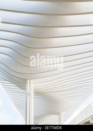Minimalist modern architecture featuring a white wavy ceiling canopy with repeating horizontal lines and slender columns, conveying rhythm, lightness Stock Photo