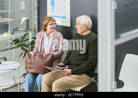 Senior Couple Waiting and Talking in Medical Office Reception Area Stock Photo