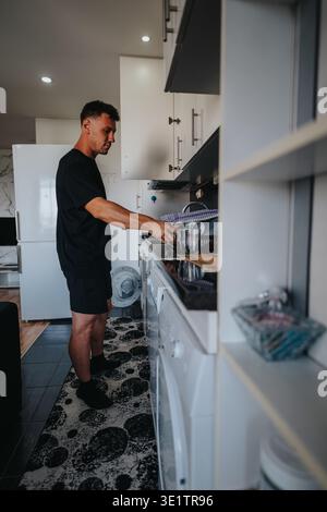 Man washing dishes at home in a modern kitchen while placing a glass in a drying rack Stock Photo