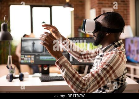 Creative individual with raised hands, using vr editing software to streamline and arrange footage. Black man seated home office desk, producing cinematic content with immersive virtual reality tools. Stock Photo