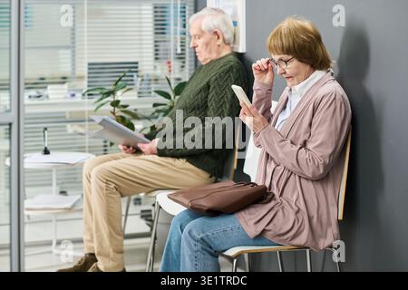 Senior Woman Using Smartphone While Senior Man Reading Documents Stock Photo