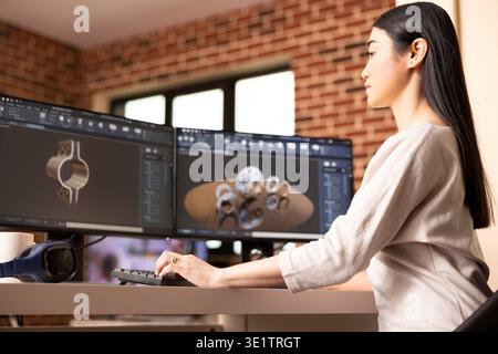Focused female remote worker designing metal components using CAD software on desktop monitors. Industrial product asian developer analyzing 3D models on computer in brick wall home. Stock Photo