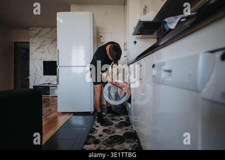Man doing laundry at home loading a front-load washing machine in a modern kitchen Stock Photo