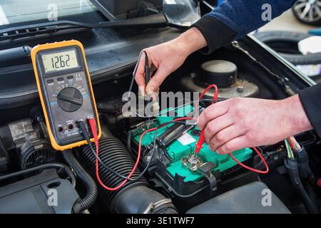 An automotive multimeter is used to check the voltage of a car battery. Stock Photo