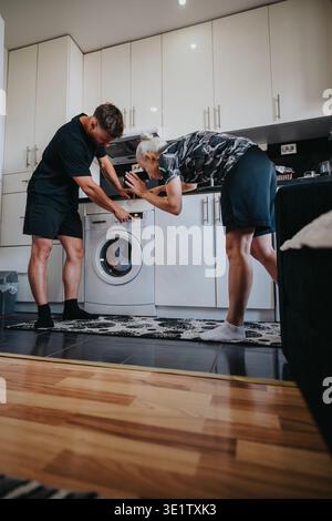 Young couple checking a front-load washing machine while doing laundry in their kitchen at home Stock Photo